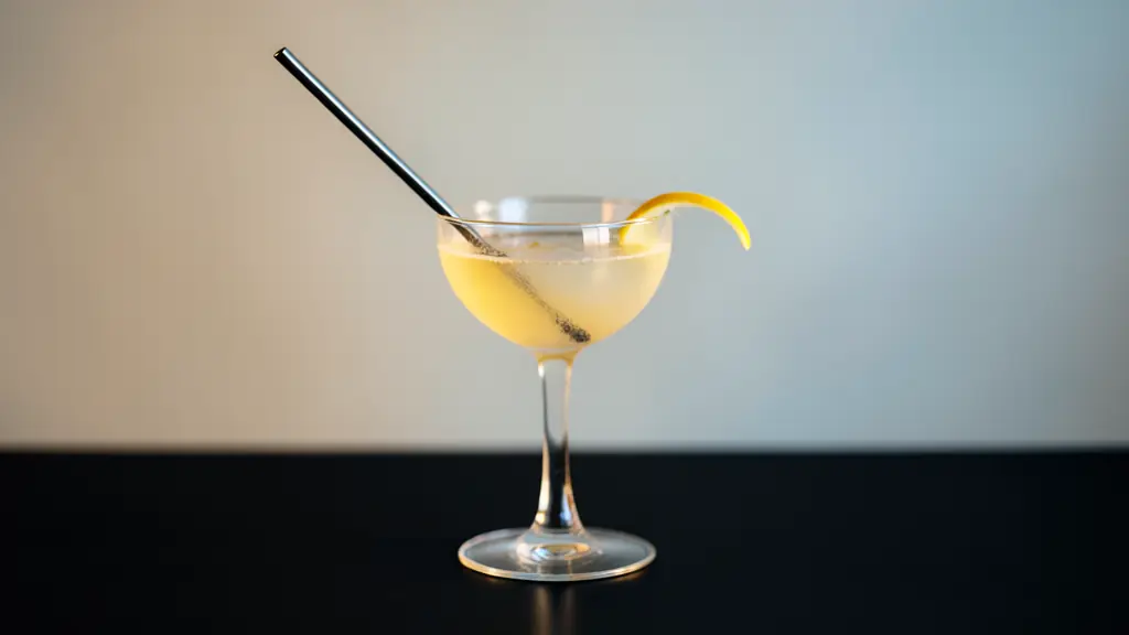 Editorial cocktail photograph with a diagonal bar spoon, curved citrus peel leading toward the illuminated rim, and controlled negative space on a dark surface